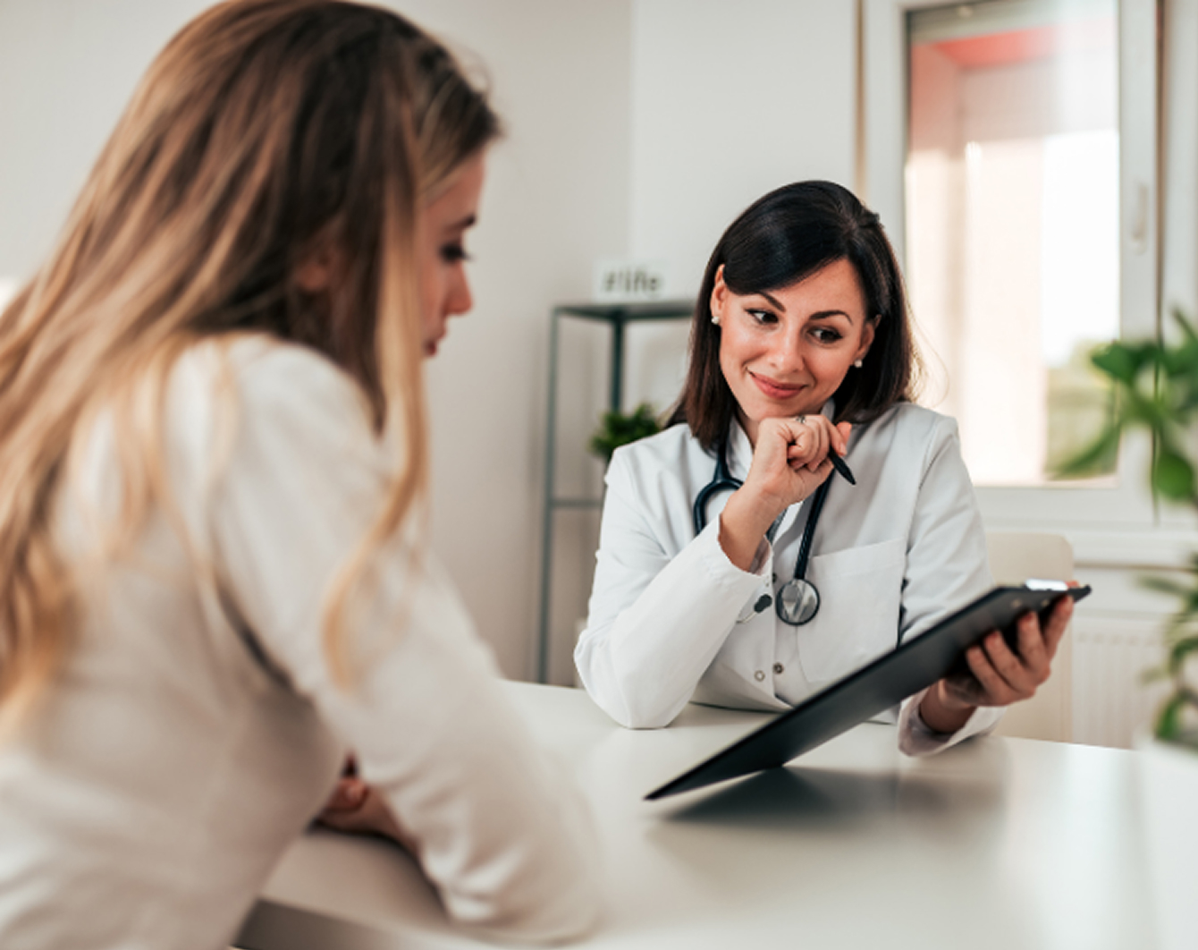 Doctor consulting patient at Hope Media House clinic, holding clipboard and pen, in a bright, welcoming office setting.